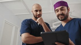 Two male surgeons of African and European descent review a tablet together in an operating room, discussing patient data. Surgeons in Operating Room - Powered by Shutterstock - Get 15% off with code: PIKWIZARD15