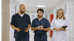 A diverse group of healthcare professionals, including doctors and nurses, walk and collaborate in a hospital hallway setting, engaged in a discussion. Medical Team Discussing Patient Records - Powered by Shutterstock - Get 15% off with code: PIKWIZARD15