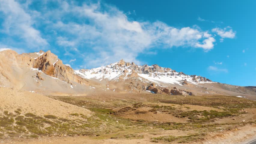 Landscape shot of snowy Himalayan mountain peaks with clouds against the blue sky as seen from Sarchu in Leh Manali Highway, India. Scenic view of dry mountain peaks with snow on top at Ladakh.