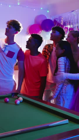 Vertical video: Diverse friends gathering at pool table dancing to music cues celebrating birthday. Party, celebration, friendship, entertainment, vibrant, social, vertical video