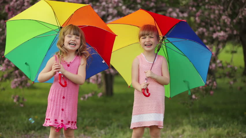 Two little girls with umbrellas laughing

