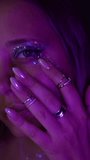 Close-up of a young mesmerising cosmic woman touching her cheek with glitter makeup under purple neon light. Alien beauty, chrome almond nails, rings and a starseed soul energy - Powered by Shutterstock - Get 15% off with code: PIKWIZARD15