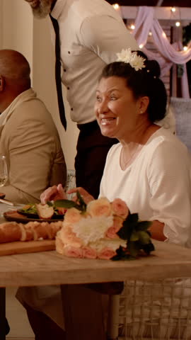 Vertical video: Mature woman talking by roses then rising as server popping cork for toast on patio. Celebration, elegance, sophistication, evening, socializing, floral, vertical video