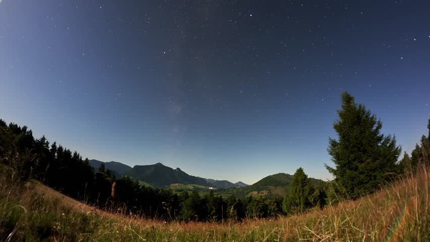 Timelapse of Starry Night Sky with Moon Over Mountain Valley and Forest Hills in Scenic Landscape