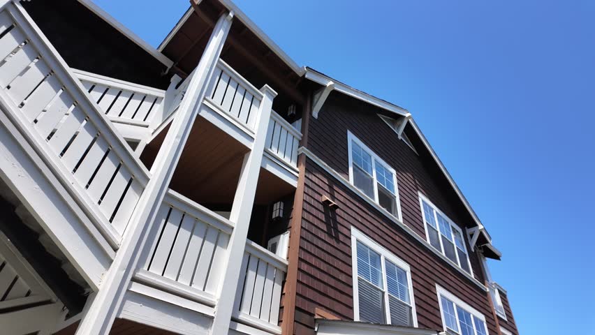 A large brown house with a white railing on the front steps. The house has a lot of windows and a balcony