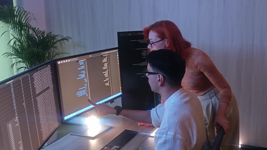 Two developer or programmer colleagues collaborating on programming and data analysis using monitors. They discuss code review system logs and share ideas in a modern office. Teamwork and technology. - Powered by Shutterstock - Get 15% off with code: PIKWIZARD15