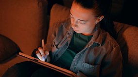Slow motion of serious Caucasian woman drawing with stylus on tablet sitting on the sofa at home in the evening. Pretty young adult lady works on digital device using special stick. Design occupation. - Powered by Shutterstock - Get 15% off with code: PIKWIZARD15