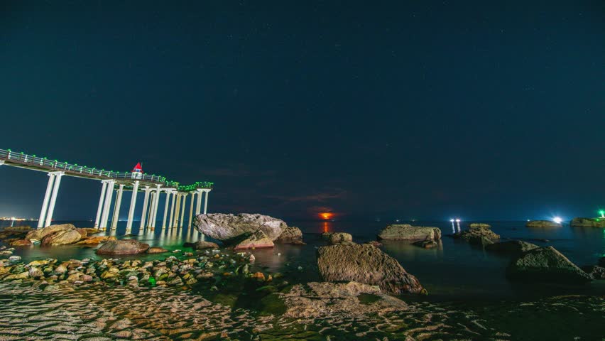 4K Timelapse zoom in on the moonrise at night, ocean waves, rocks, and the Igari Anchor Observation Deck, an anchor in the middle of the ocean, Pohang, South Korea.