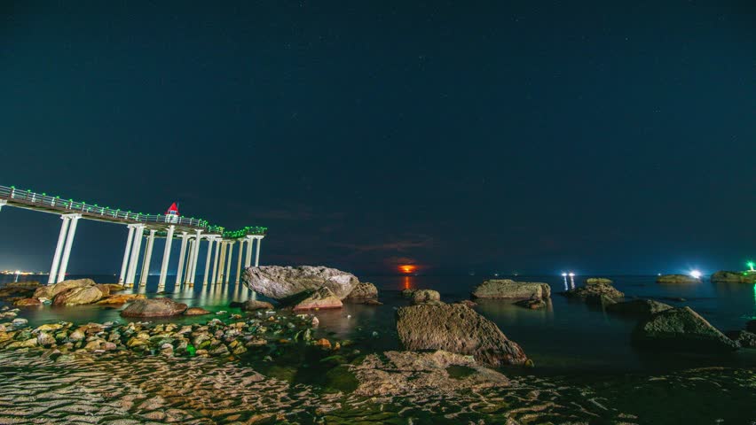 4K Timelapse: Moonrise at night, sea waves, rocks, and the Igari Anchor Observation Deck, an anchor in the middle of the ocean, Pohang, South Korea.