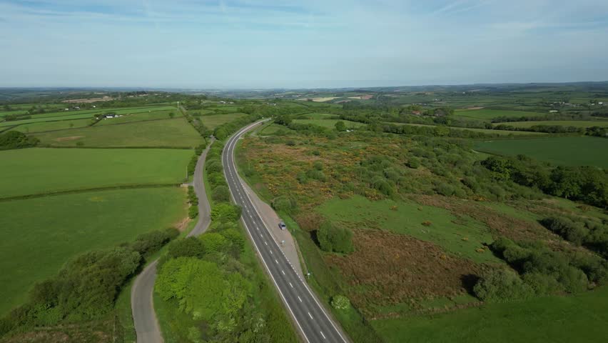 Aerial view of South Downs, Hampshire, England – a winding rural road weaves through patchwork fields, hedgerows, and rolling hills, showcasing the charm of the English countryside under a clear sky.