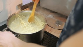 Close-up of a pot with spaghetti cooking in boiling water on a stove. A hand stirs the pasta with a wooden spoon. Home kitchen scene focused on cooking process and steam rising from the pot - Powered by Shutterstock - Get 15% off with code: PIKWIZARD15