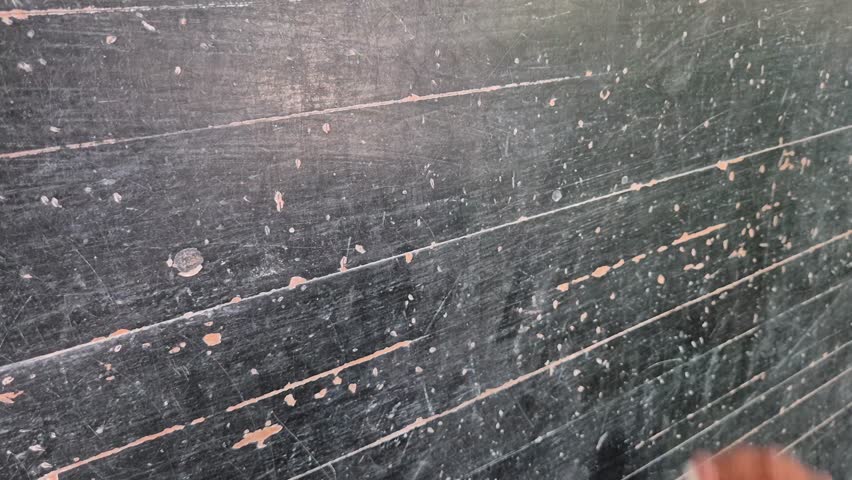 The hand of an elementary school girl is writing the letter abc on the blackboard.