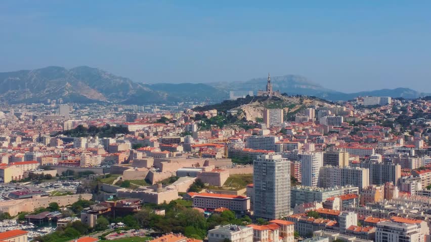 aerial view of the vibrant city of Marseille, France, showcasing its iconic landmarks including the majestic Notre Dame de la Garde basilica perched atop a hill, the bustling Old Port, and the dense u