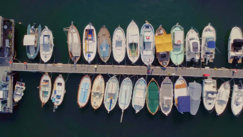 An aerial top down view captures the serene beauty of a bustling marina in Marseille, France, with numerous boats neatly docked along a pier on calm, turquoise waters.