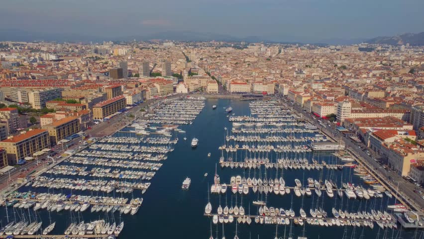 An expansive aerial view showcases the historic Old Port (Vieux-Port) of Marseille, France, bustling with numerous sailboats and yachts docked in the marina.