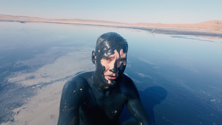 The guy smears himself with therapeutic mud and prepares to plunge into it. Mud lake with healing mud. Natural patience.