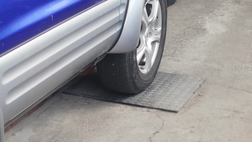 A used car's wheel being shaken by a road simulator or shaker plate during technical inspection. Close up, looking down shot, real time, no people