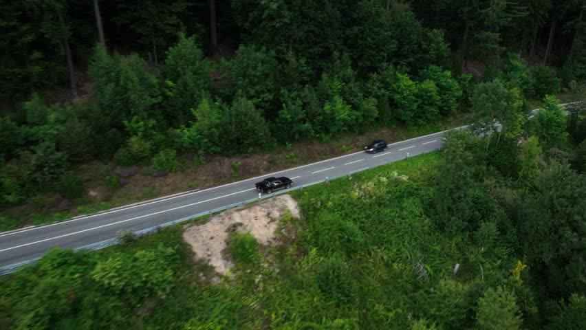 Aerial view tracking a old sports car driving on a forest road, gloomy day