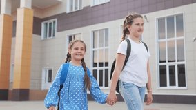 girls walking to school holding hands smiling with backpacks on older sister leading younger while younger points toward modern school building conveying friendship and safe walk routine together - Powered by Shutterstock - Get 15% off with code: PIKWIZARD15