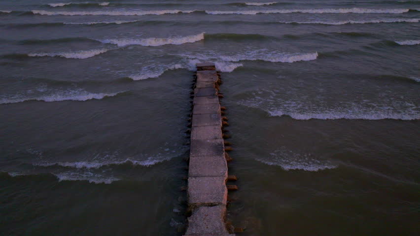 Drone aerial looking straight down over a concrete pier in Lake Michigan with a slow push forward as gentle waves roll in against the shoreline.