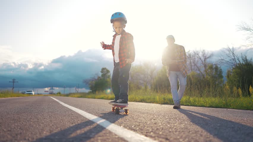 Two young boys on a skateboard. A father and child skateboarding outdoors. A helmet for road bonding sport. Two young children riding lifestyle a skateboard.