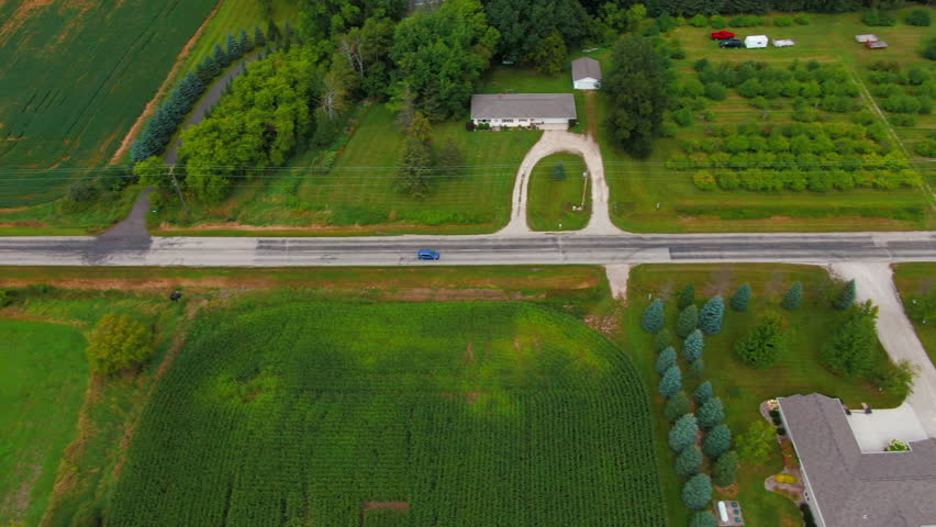 Aerial Tracking Shot of Blue Car Traveling Down Rural Farmland with Homes Wisconsin
