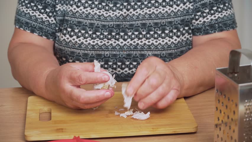 Peeling garlic cloves for cooking Ukrainian borscht. Removing dry skin from fresh garlic for preparing traditional soup. Cleaning aromatic cloves for making borscht recipe. Preparing garlic ingredient