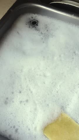 Hygienic person washing dishes in foamy soapy water Vertical shot