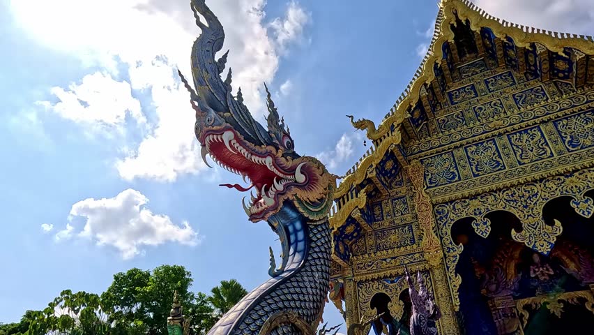 Low angle view and panning right to the blue and gold intricate detailed design of Wat Rong Suea Ten or Blue Temple in Chiang rai Thailand