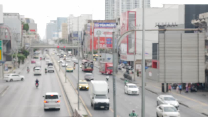 Blurred daytime view of Bangkok street with moving traffic and vehicles.