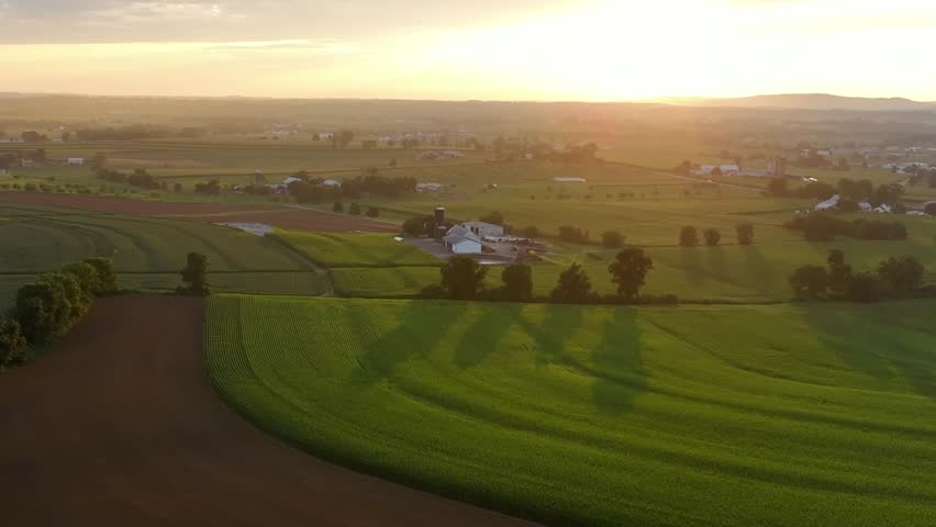Golden hour over American countryside farm fields with farmhouses. Beautiful picturesque suburb landscape in rural area of USA in summer. Aerial wide shot. Pennsylvania, u.s.