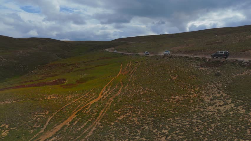 Aerial view of the winding Deosai Park Road cutting through green meadows under a clouded sky, creating a striking contrast, Skardu, Gilgit Baltistan, Pakistan.