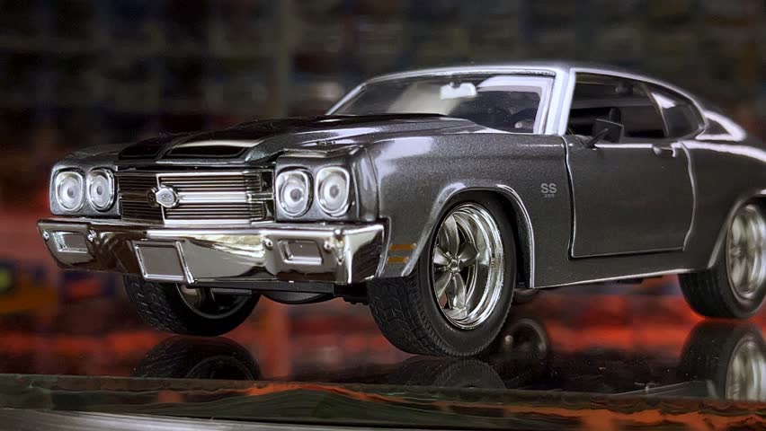 Zoom out of detailed black diecast muscle car model with chrome accents, spinning on mirror.