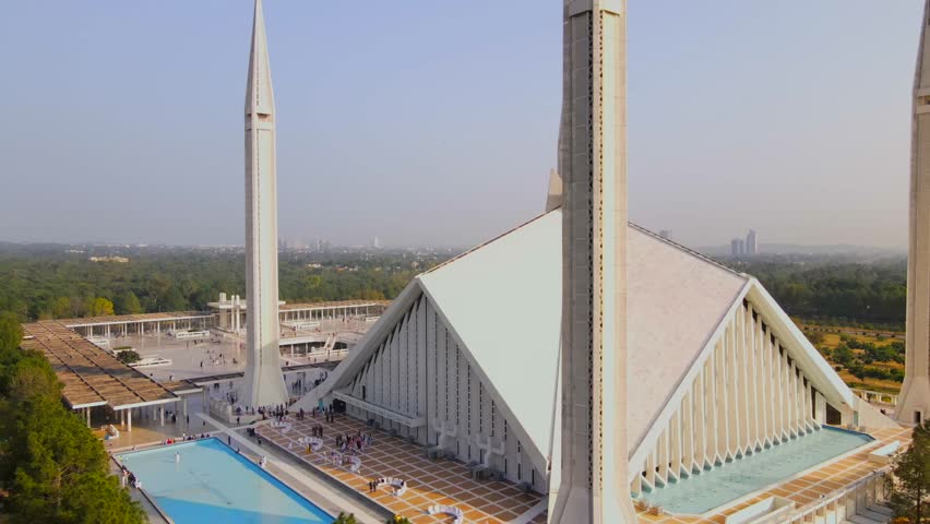 Aerial view of Faisal Mosque's grand architecture with its angular roofs and towering minarets, contrasting with the lush greenery, Islamabad, Islamabad Capital Territory, Pakistan.