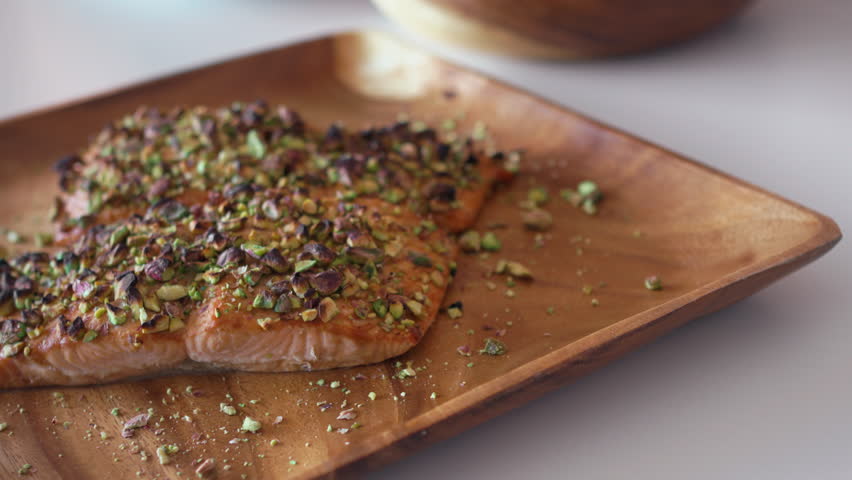 Grilled salmon fillets topped with crushed pistachios served on wooden plate. Delicious and healthy dish highlighting the combination of fish and nuts for nutritious meal