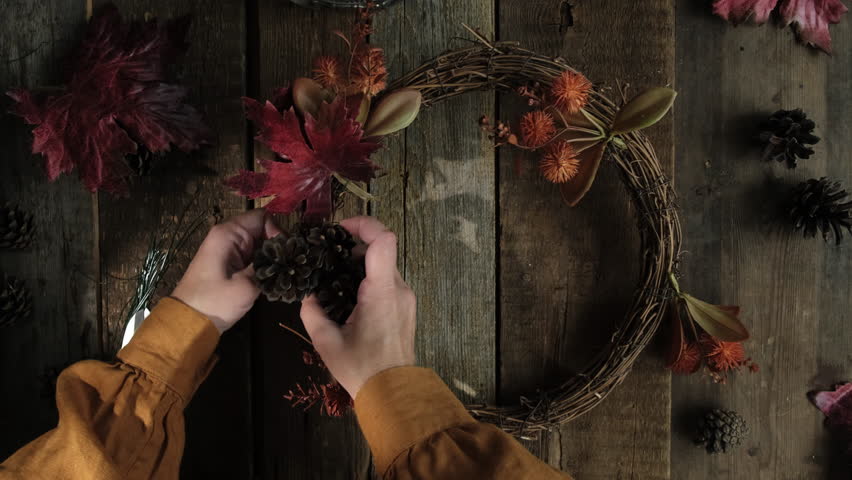 DIY fall wreath. Hands making autumn wreath using red leaves and cones. Overhead shot