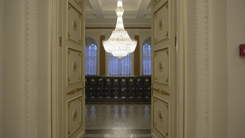 Rich carved doors open pompous hall glowing with chandelier brilliance. Heavy adorned doors reveal lavish hall filled with splendor