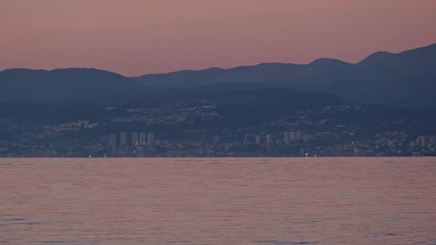 Typical old panel apartments in pink sunset lights. Block houses of Rijeka, Croatia with the Adriatic Sea in the foreground. There are the Grobnicke Alps Mountains in the background.