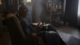 Elderly retired woman looks at old framed picture sitting in vintage armchair. Senior female pensioner remembers past times with photo staying at home - Powered by Shutterstock - Get 15% off with code: PIKWIZARD15