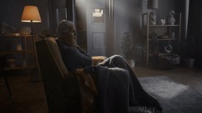 Senior woman with warm blanket sits alone in vintage armchair at home. Elderly lady suffers from loneliness and depression symptoms in twilight living room - Powered by Shutterstock - Get 15% off with code: PIKWIZARD15