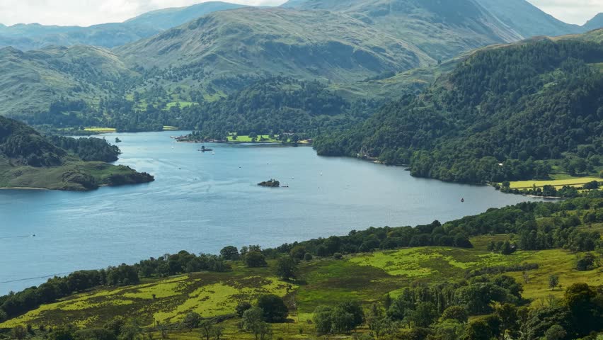 Sideways panning drone view of Ullswater lake, islands and fells in summer.