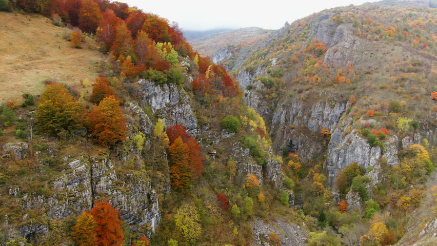 Hills with trees showing fall colors Rock formations are visible on the sides of the hills The sky is a light color