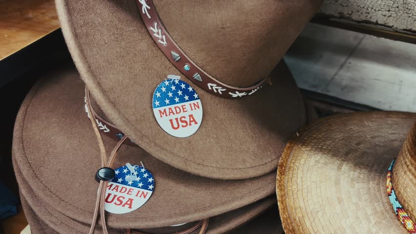 Brown cowboy hats with leather bands and patriotic made in usa stickers stacked on display