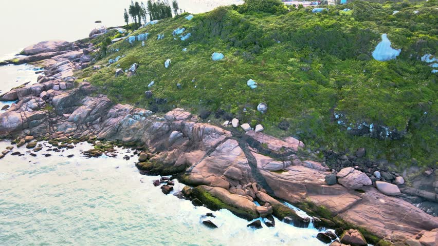 Joaquina Beach seen from above, an aerial view of the rocky coastline with Atlantic Forest and turquoise ocean with many mountains and dunes on the horizon in Florianopolis, Santa Catarina, Brazil.