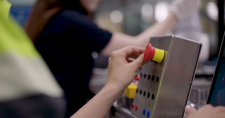 female engineer pressing emergency stop button during automation training session to test robot safety function while operating robotic arm on manufacturing control panel in smart industry40 lab
