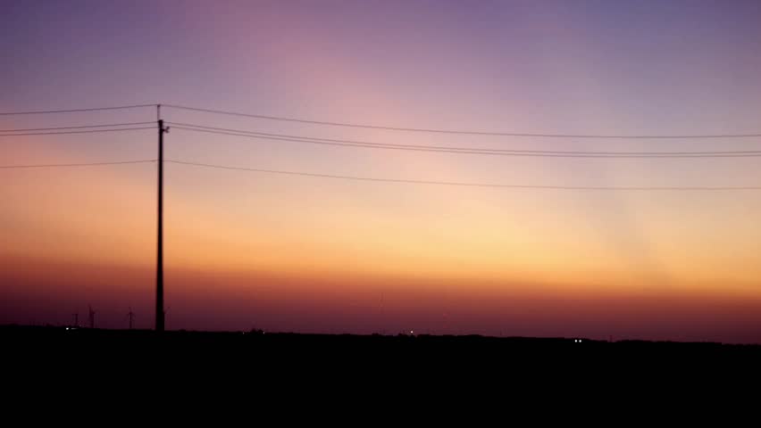 POV drive along a rural road under construction at colorful sunset with telephone poles silhouetted against the colorful sky. Great for road trip, travel, or Americana themes.