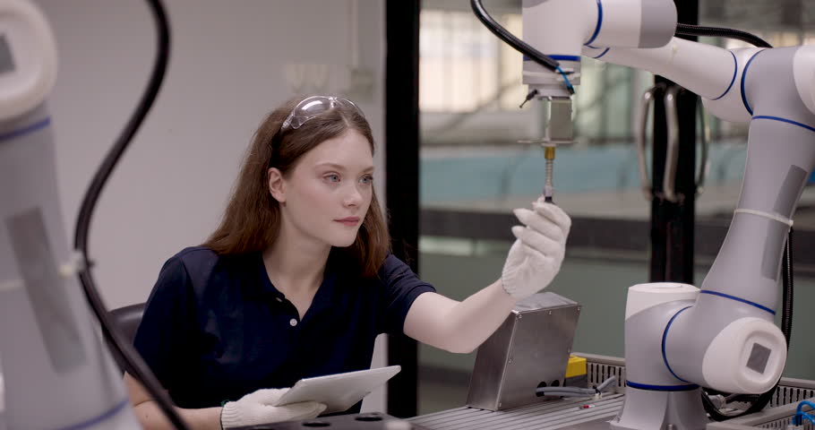 female student operating robotic arm using tablet while observing object placement during automation lab class focused on precision robotics calibration inside high tech industry40 learning facility