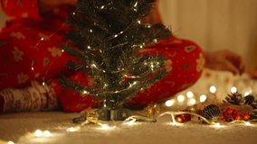 Woman in Santa Hat Wrapping Lights Around Top of Mini Tree in Warmly Lit Room with Curtains in Background. - Powered by Shutterstock - Get 15% off with code: PIKWIZARD15