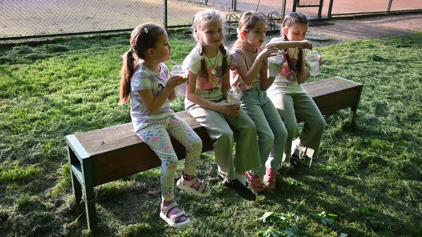 Four Happy Young Girls Enjoying Refreshing Drinks Outdoors on a Sunny Day