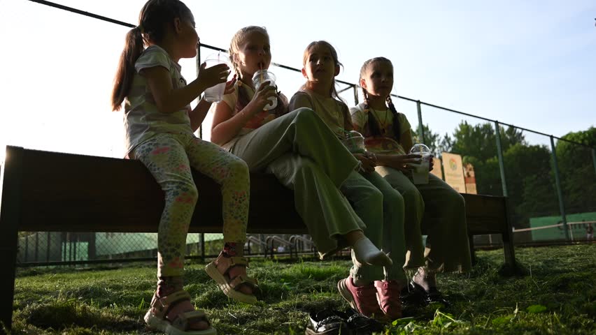 Four Happy Young Girls Enjoying Refreshing Drinks on a Bench at a Sunny Outdoor Park